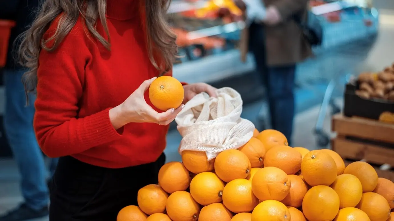 Eine Frau sammelt Orangen in einer wiederverwendbaren Tasche; Ökologie- und Earth-Day-Thematik.